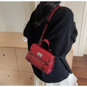 Detailed view of red retro handbag with floral embroidery and gold metal twist lock closure