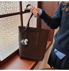 Detail of dark brown suede tote bag with blue wooden horse charm by a window