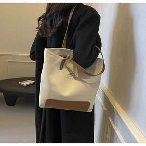 Detailed side view of off-white canvas tote bag with brown leather handles worn by a model