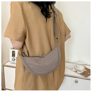 Rear view of a grey nylon crescent messenger bag on a model in a cozy kitchen setting