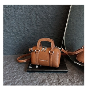 Vue détaillée du mini sac marron grainé avec fermetures éclair argentées sur un livre