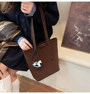 Detail of dark brown matte tote bag with small horse charm and dual top handles