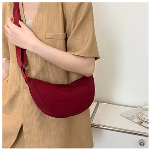 Detail shot of a burgundy nylon half-moon crossbody bag worn by a model in casual style