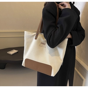 Detailed shoulder view of a canvas tote bag with brown leather straps and Slogan print