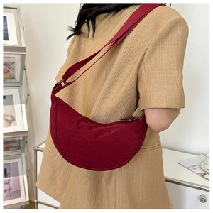 Detail of burgundy half-moon nylon crossbody bag worn with a casual camel blazer