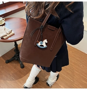 Close-up of a brown suede bucket bag with a small blue and white horse charm detail
