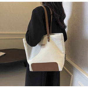 Detail of off-white canvas tote bag with brown leather strap and rivet attachment