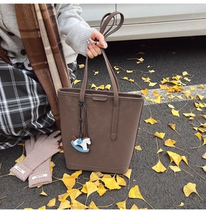 Detail of dark brown tote bag with felt texture and cute blue horse charm accessory