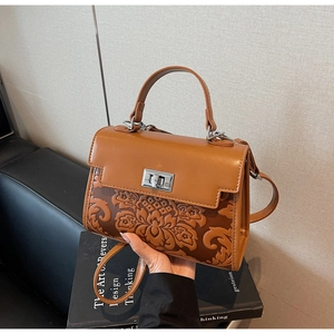 Detailed close-up of brown faux leather handbag featuring floral embossing and silver twist lock