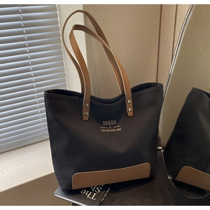 Detail of minimalist black canvas tote bag with brown leather handles and brand lettering