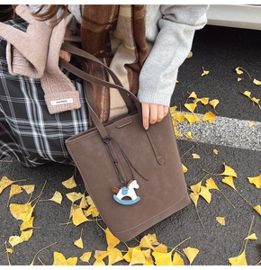 Dark brown suede tote bag with horse charm on ginkgo leaf ground in autumn