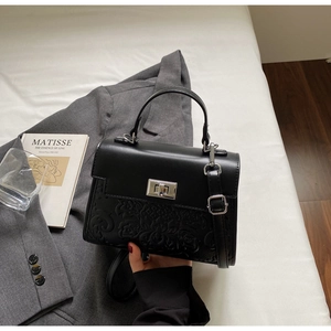 Detail of black leather handbag with embossed patterns and silver rotating metal lock