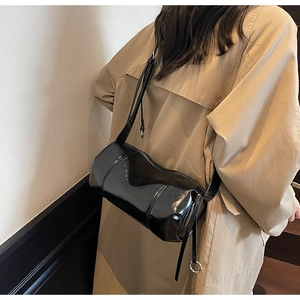 Side view of black patent leather cylinder crossbody bag on a trench coat model