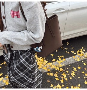 Detail of dark brown matte tote bag with small horse charm on an autumn street background