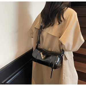 Detail of a black glossy cylindrical pillow bag showing the sleek patent leather texture