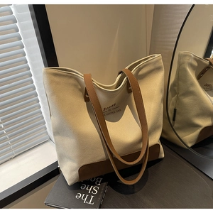 Close-up of beige canvas tote bag with brown leather handles and printed text