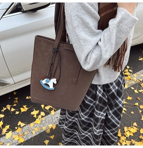 Detail of dark brown matte leather tote bag featuring a cute rocking horse charm