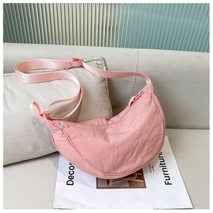 Detailed close-up of pink crescent nylon bag with adjustable strap on a sofa background