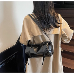 Detail of glossy black cylinder shoulder bag with reflective finish on beige trench coat
