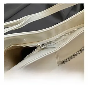 Detail of cream white faux leather bag showing silver metal zipper with branded engraving