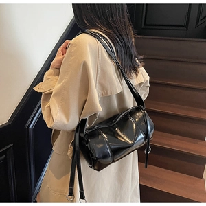 Detail of a shiny black patent leather cylinder bag worn with a classic beige trench coat