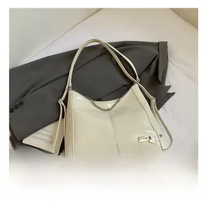 Detail of creamy white large crescent tote bag with decorative silver chains and heart charm