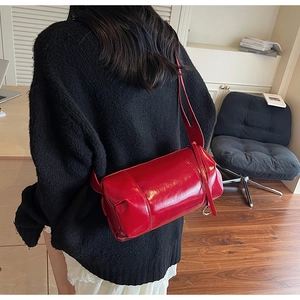 Detail of glossy red cylindrical shoulder bag showing leather texture and metal rings