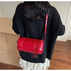 Close-up of a glossy red cylinder bag with silver ring detail on a model's shoulder