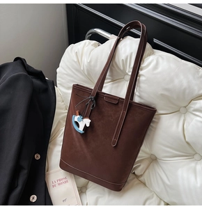 Detail of dark brown suede tote bag with long strap and blue wooden horse charm