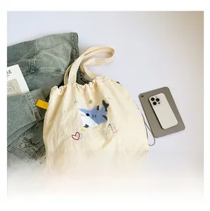 Detail der cremefarbenen Segeltuchtasche mit blauer Hai-Stickerei und Good Luck Text