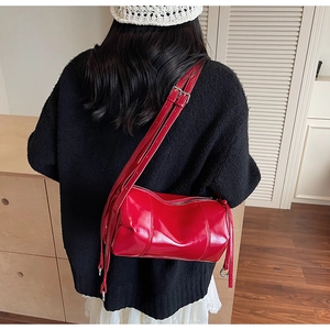 Detailed view of glossy red barrel shoulder bag being worn by a model in casual setting