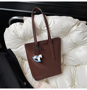 Detail of dark brown leather tote bag with a small horse charm on a white sofa