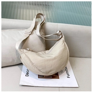 Detail of a beige nylon crescent bag styled on a sofa with magazines for lifestyle look