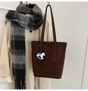 Brown textured bucket bag with a blue horse charm displayed in an autumn lifestyle setting
