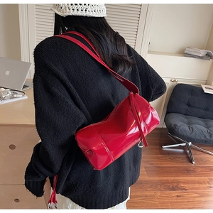Detailed close-up of a red patent leather cylinder bag worn over the shoulder