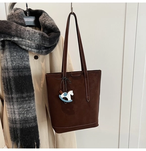 Detail of dark brown suede tote bag with a horse charm hung on a coat rack stylishly