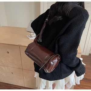 Detail view of a large dark brown cylinder shoulder bag worn over a black sweater