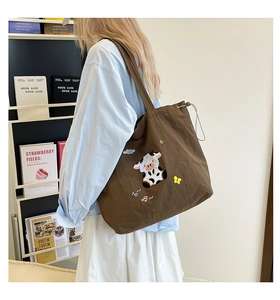Detail einer dunkelbraunen Canvas-Tasche mit süßer Kuh-Stickerei und Kordelzugverschluss