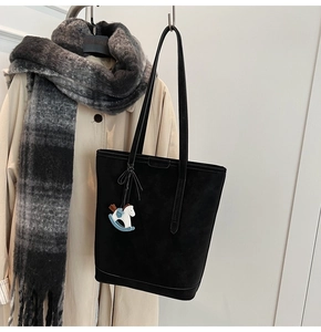 Detail of black suede tote bag with horse charm, paired with stylish autumn trench coat