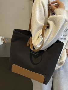 Black canvas tote bag with brown leather handles and 'BE THE BETTER ONE' text print