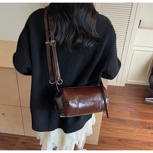 Detailed close-up of dark brown cylinder bag with polished oil wax leather texture and strap