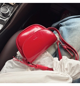 Détail d'un sac selle rouge brillant avec logo et bandoulière dans un habitacle de voiture