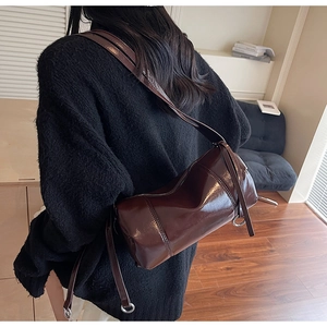 Detail of a brown glossy cylindrical shoulder bag with adjustable strap and metallic rings