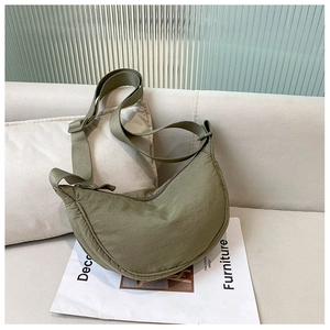 Detail of army green nylon crescent bag with adjustable strap on a minimalist sofa