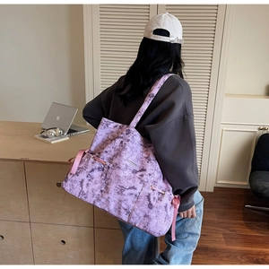 Détail du sac cabas tie-dye violet avec ruban rose et logo en métal sur la bandoulière