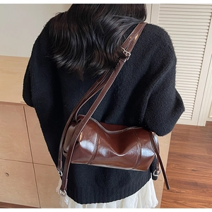 Detail of a brown cylinder crossbody bag with glossy finish and adjustable strap