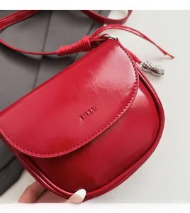 Détail du sac selle rouge avec texture en cuir brillant et pendentif cacahuète argenté
