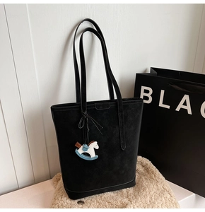 Detail of a large black matte hobo bag with a blue horse charm on a soft plush surface