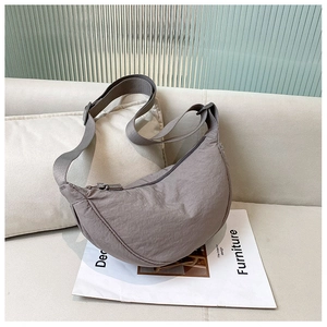 Detail view of a grey nylon crescent messenger bag on a cozy sofa with magazines