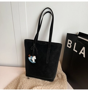 Detail view of a black matte tote bag with thin straps and a blue leather horse charm